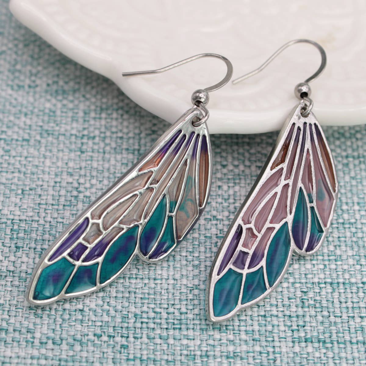 Pair of wing-shaped earrings with colorful design on a textured surface
