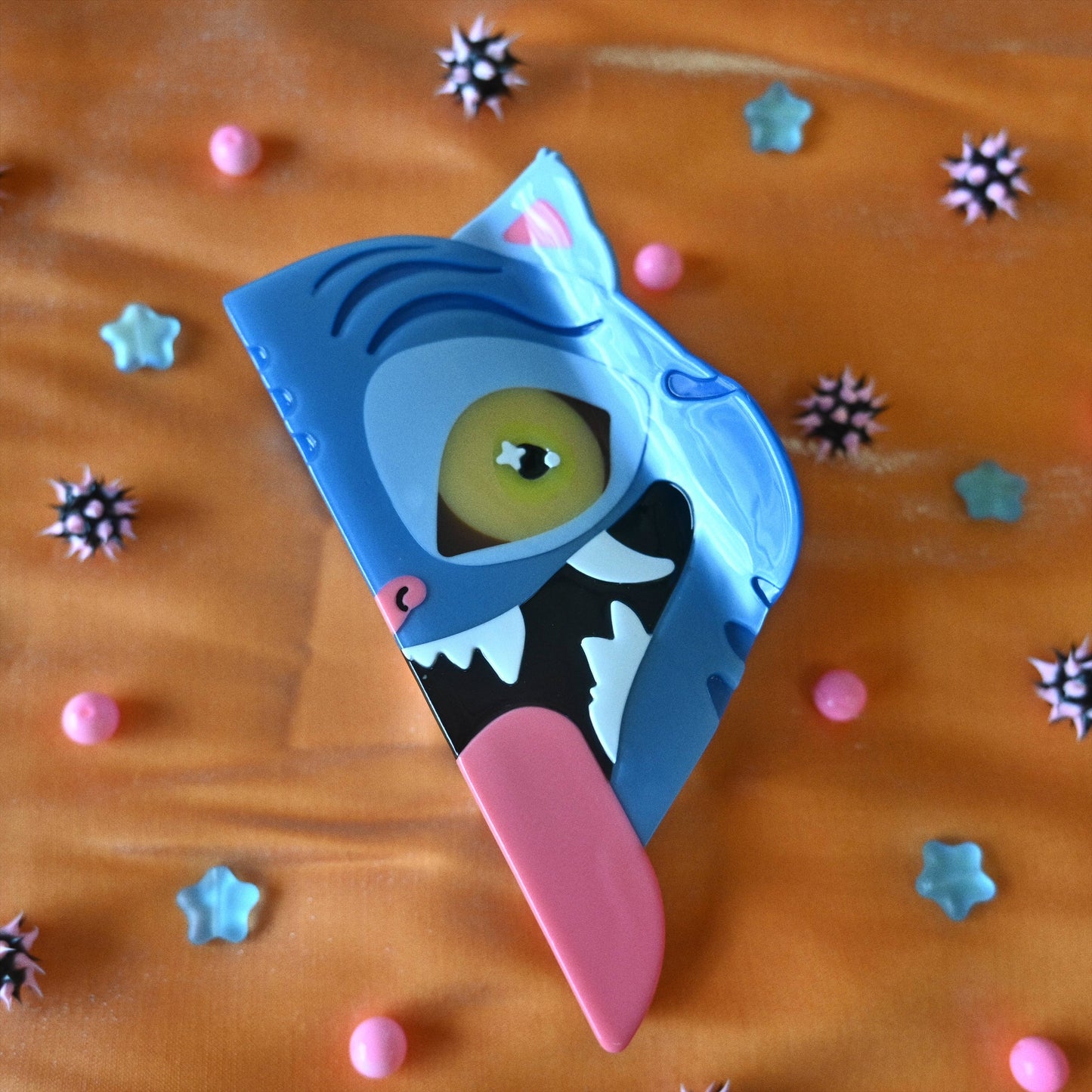 Colorful blue tiger hair claw with a pink tongue on an orange background with star-shaped objects.