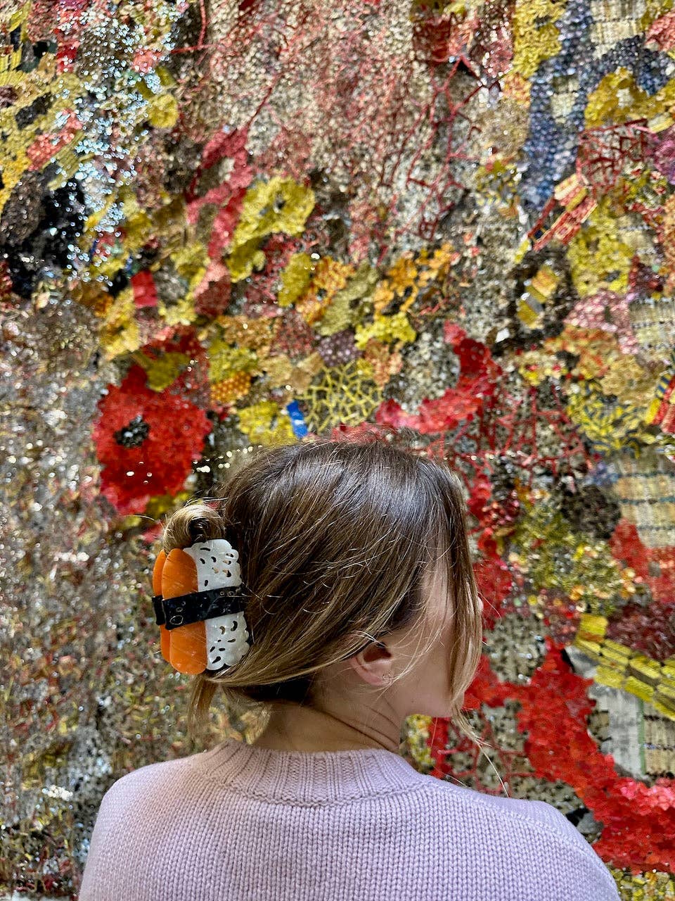 Person with a sushi hair clip in front of a colorful, textured wall.