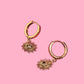 Gold hoop earrings with sunray-shaped charms on a pink background