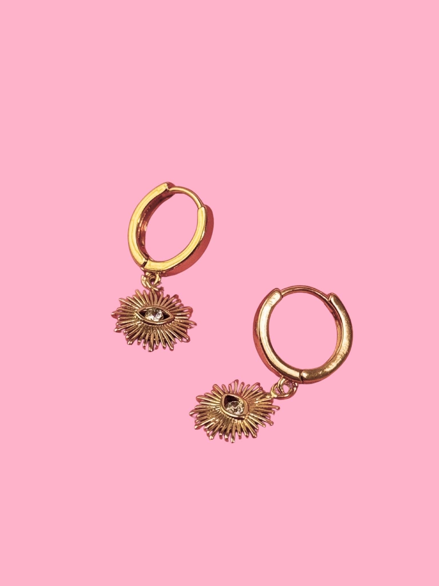 Gold hoop earrings with sunray-shaped charms on a pink background