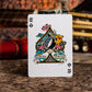 Playing card with floral design on a wooden surface with blurred guitar in the background