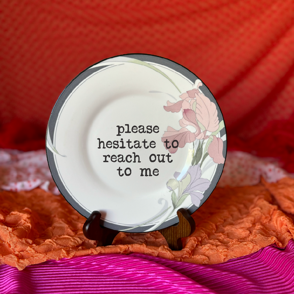 Decorative plate with floral design and text on a stand against an orange fabric background