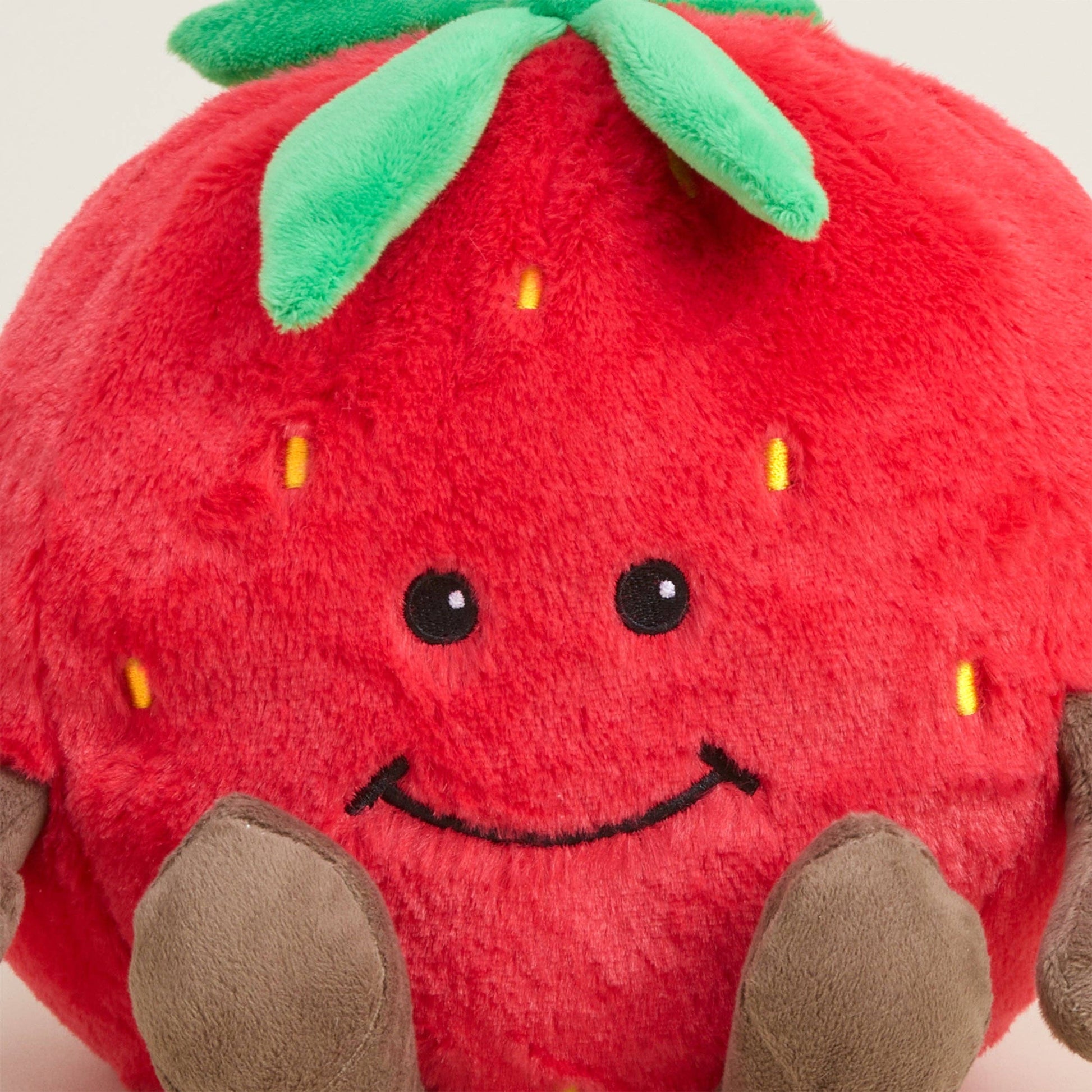 Plush strawberry toy with a smiling face on a white background