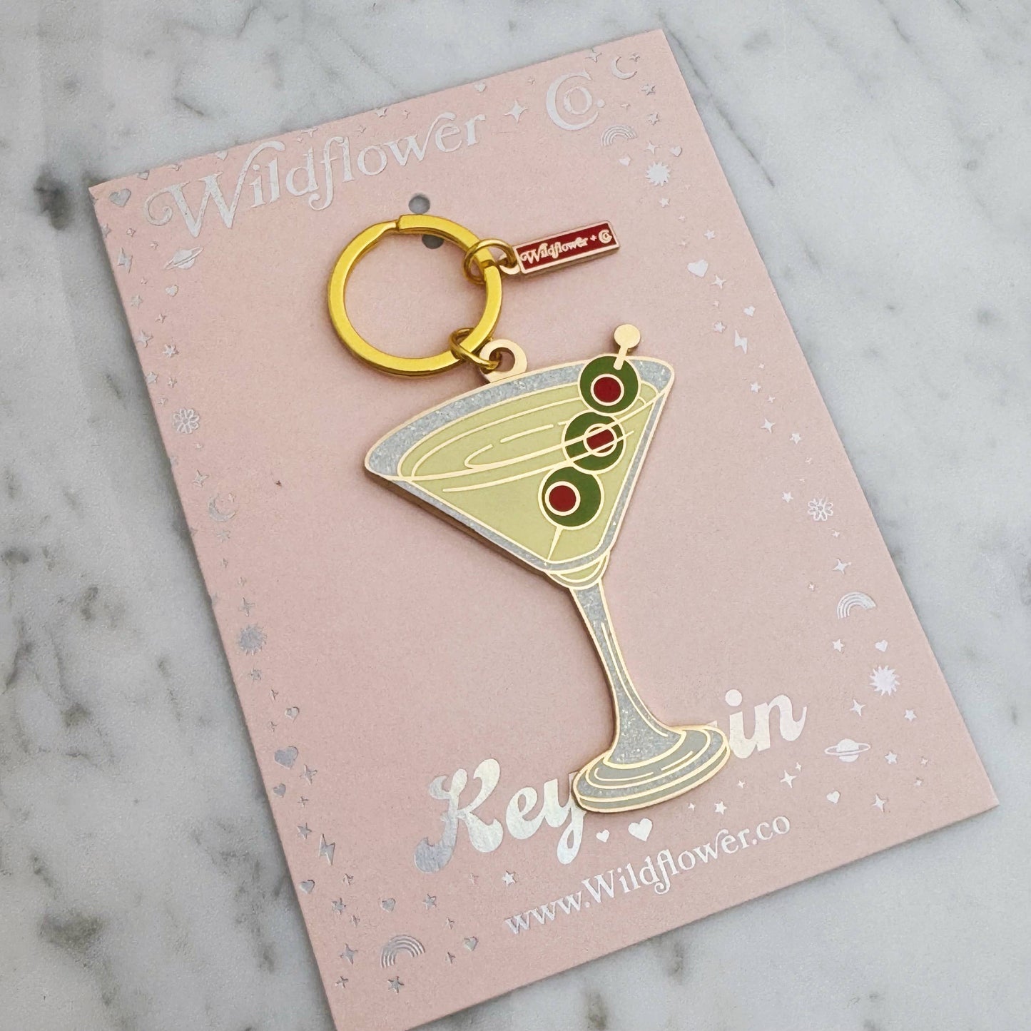 Keychain shaped like a martini glass with olives on a pink card with 'Wildflower Co' branding.
