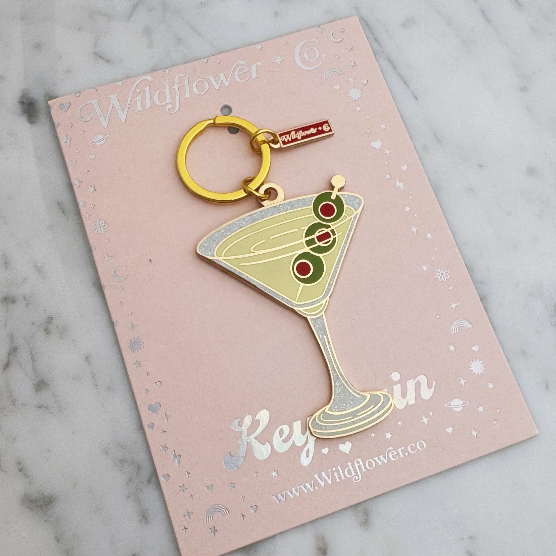 Keychain shaped like a martini glass with olives on a pink card with 'Wildflower Co' branding.