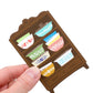 Magnet of a small wooden shelf with colorful bowls held by a hand on a white background