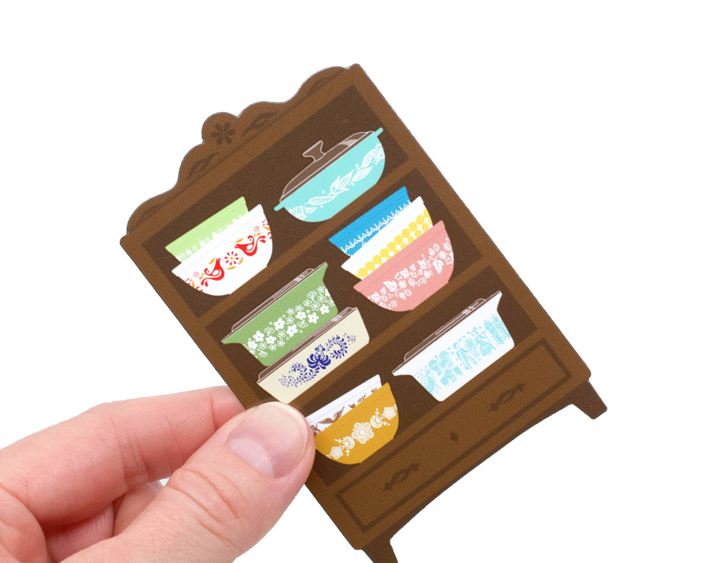 Magnet of a small wooden shelf with colorful bowls held by a hand on a white background