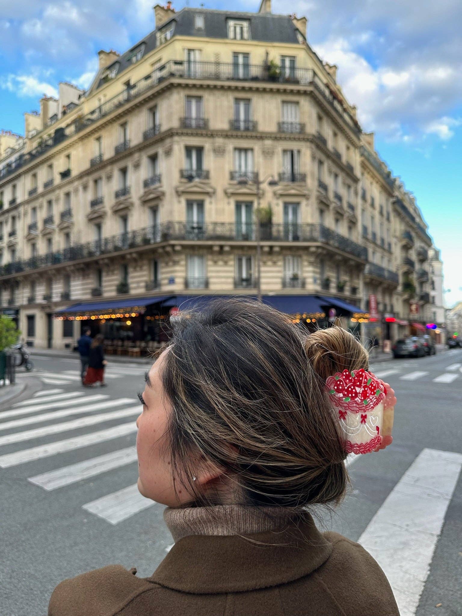 Person with a bun wearing a decorative cake hair clip in an urban street setting
