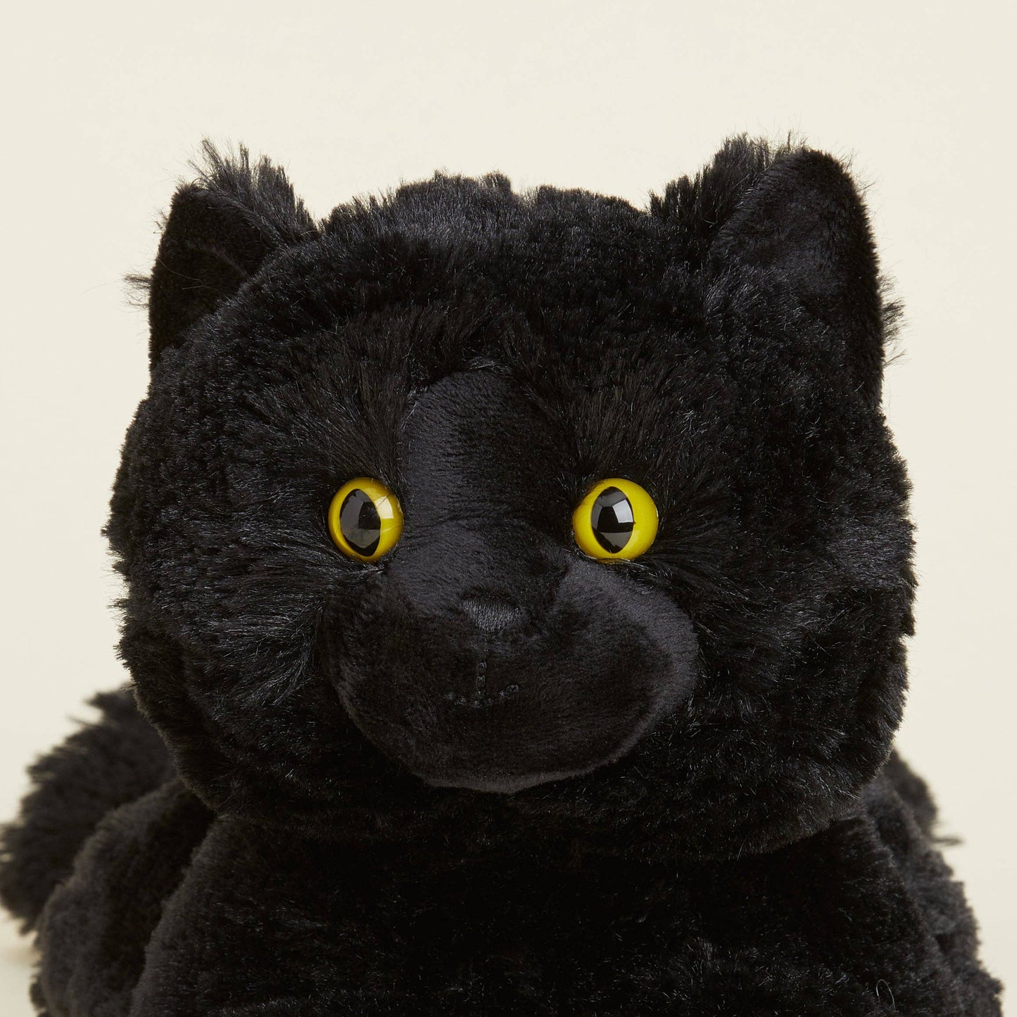 Close-up of a black plush toy with yellow eyes on a beige background