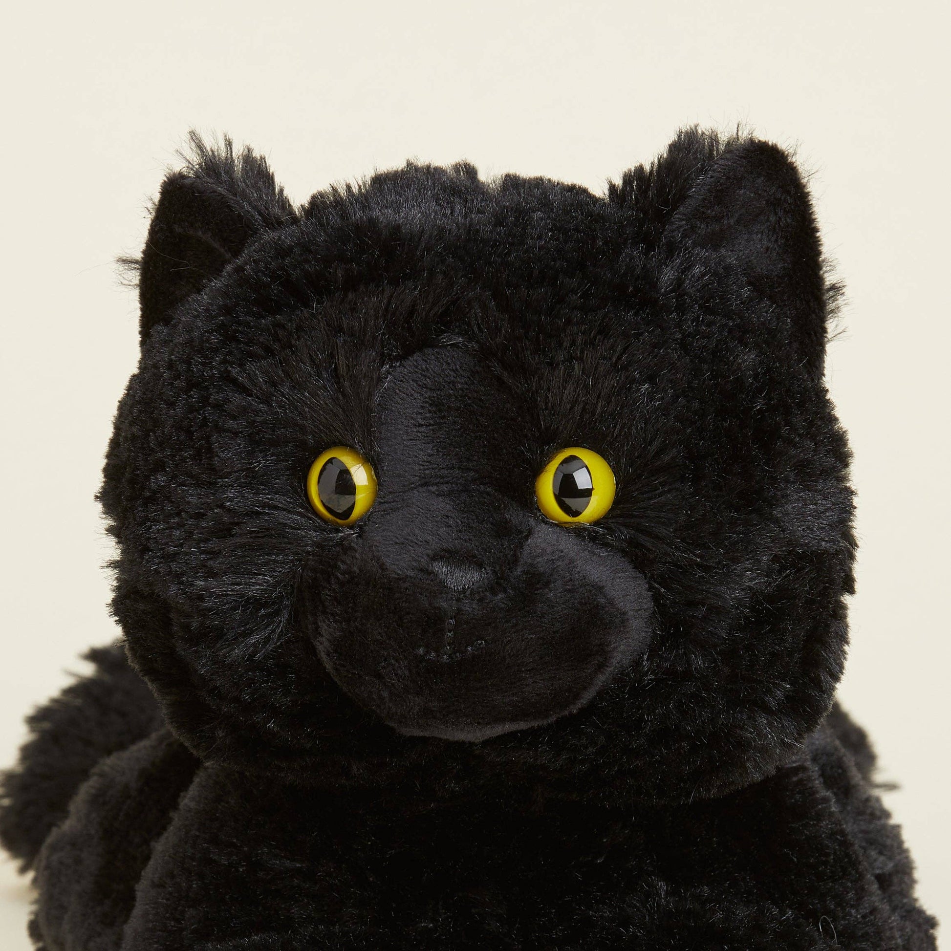 Close-up of a black plush toy with yellow eyes on a beige background