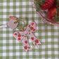 Pink bow keychain with strawberry design on a green and white checkered tablecloth.