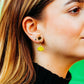 Close-up of a person wearing a yellow frog earring with a green background