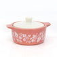 Pink pyrex ceramic dish with white floral patterns and a white lid on a white background