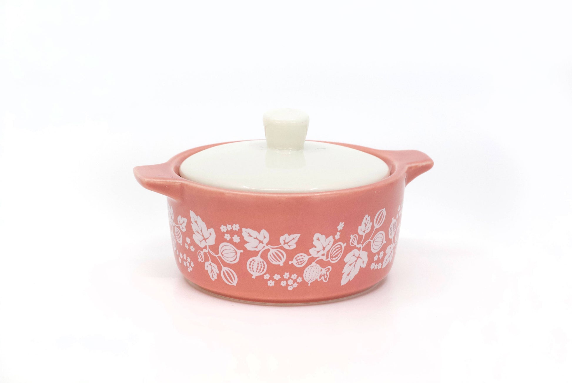 Pink pyrex ceramic dish with white floral patterns and a white lid on a white background