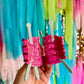 Pink knitting yarn hair clips held by a hand with a colorful fringe background