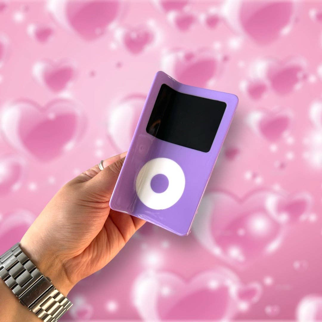 Hand holding a purple iPod nano hair claw against a pink heart-patterned background