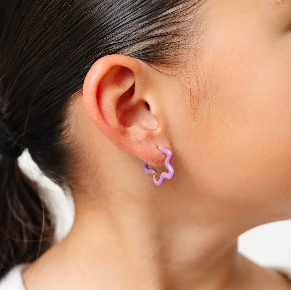 Close-up of an ear wearing a purple flower-shaped earring with a blurred background