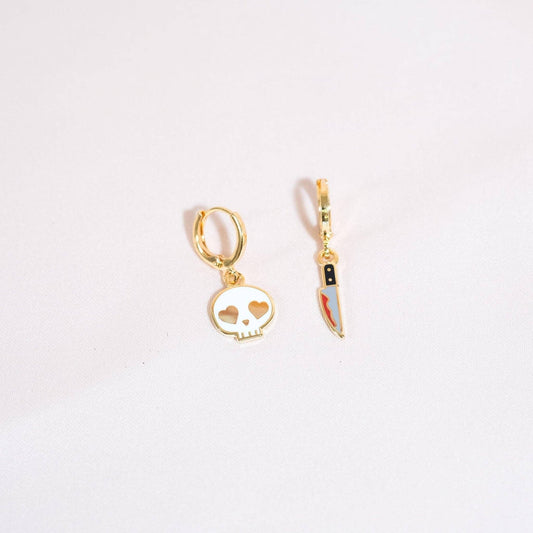 Gold skull-shaped earring with a bloody knife earrings design on a white background