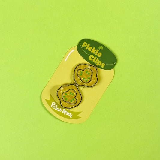 Pickle-shaped hair clips in a green container on a green background