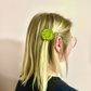 Person with a green pickle hair clip in their blonde hair against a plain background
