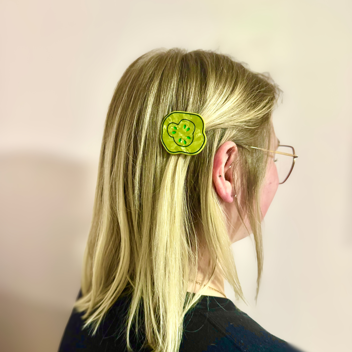 Person with a green pickle hair clip in their blonde hair against a plain background