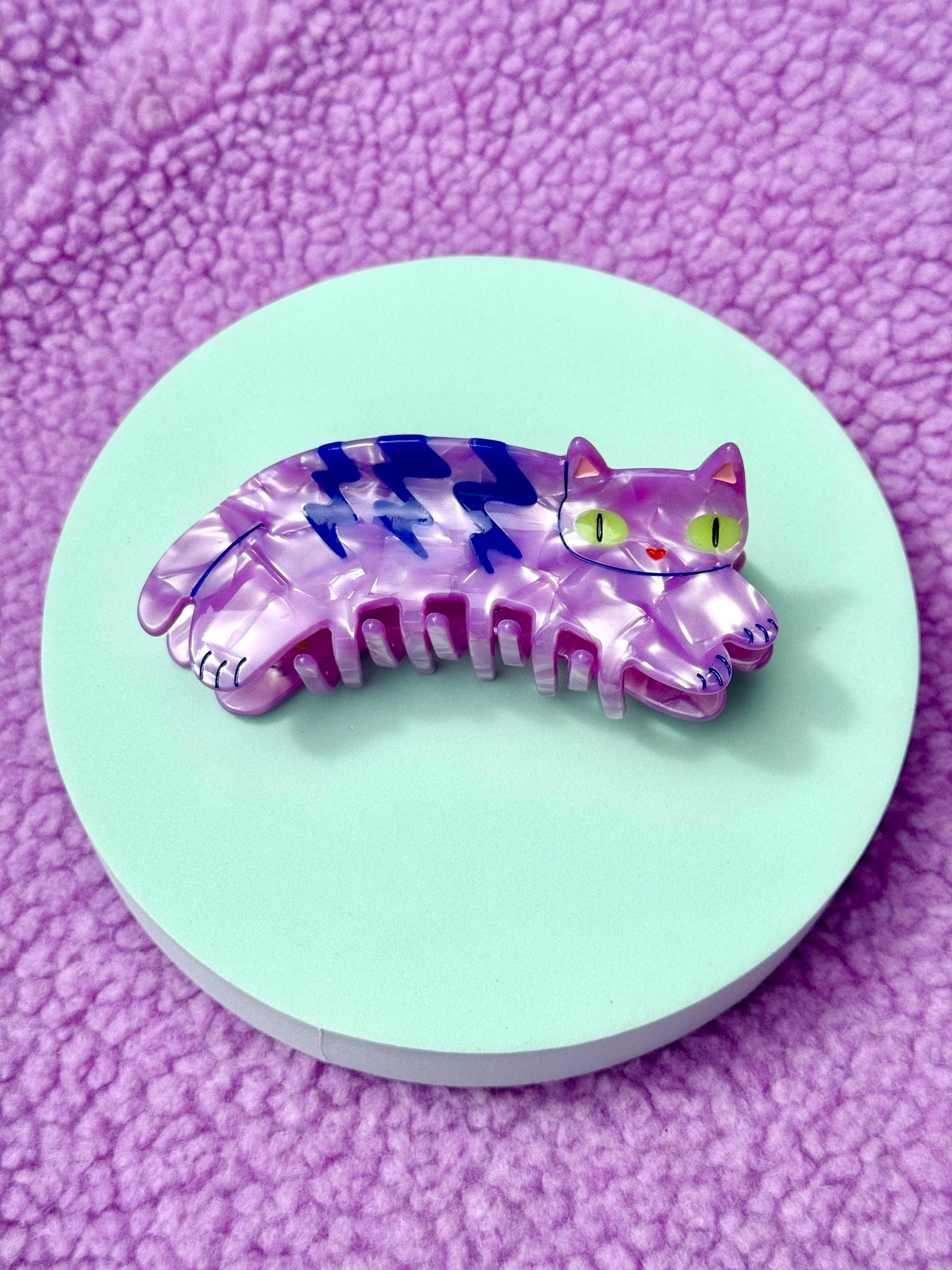 Purple and blue cat-shaped comb on a light green circular base with a purple textured background