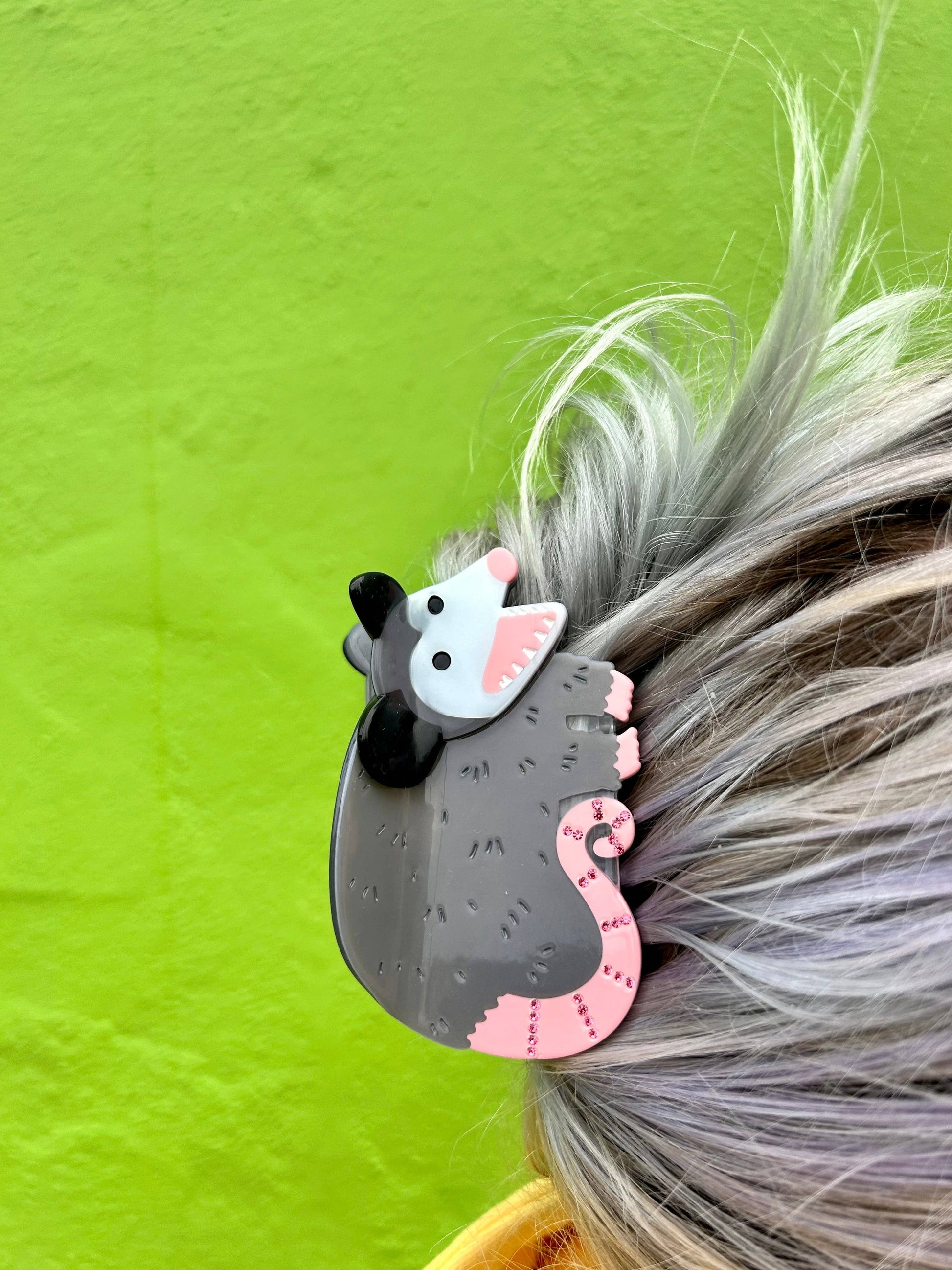 Hair clip shaped like a possum with pink accents on a person's hair against a green background