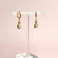 Gold cat hoop earrings on a clear stand against a pink background