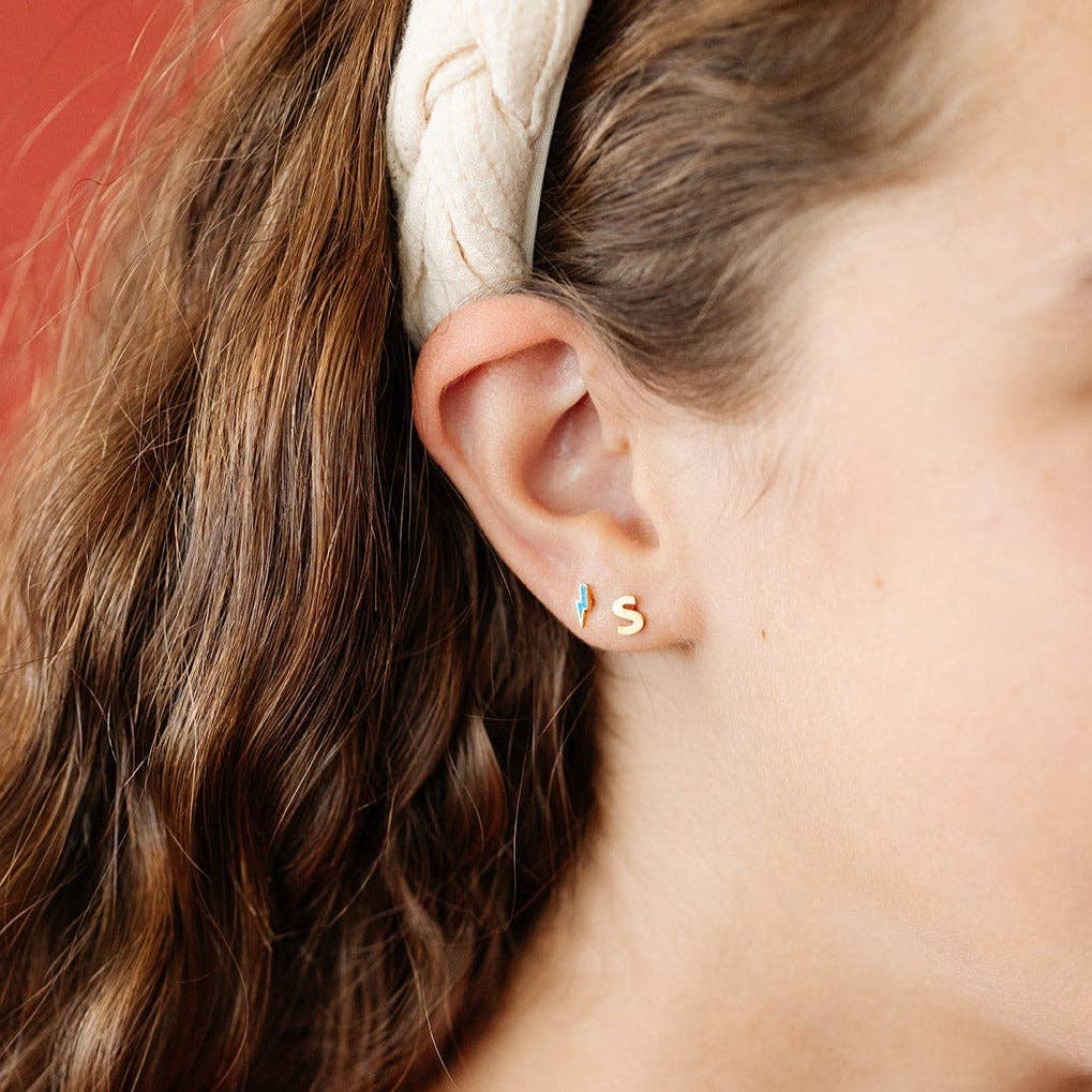 Close-up of an ear with gold earrings and a beige headband.