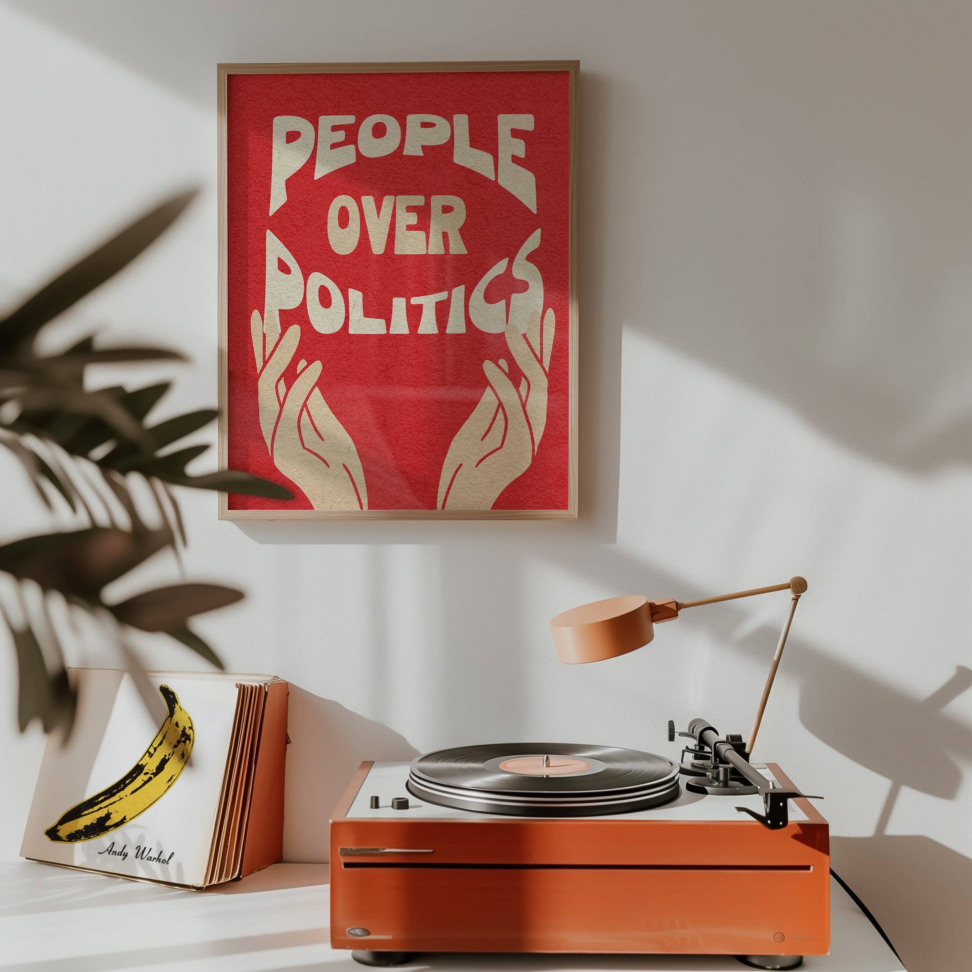 Orange record player on a white surface with a red poster reading 'People Over Politics' on the wall.