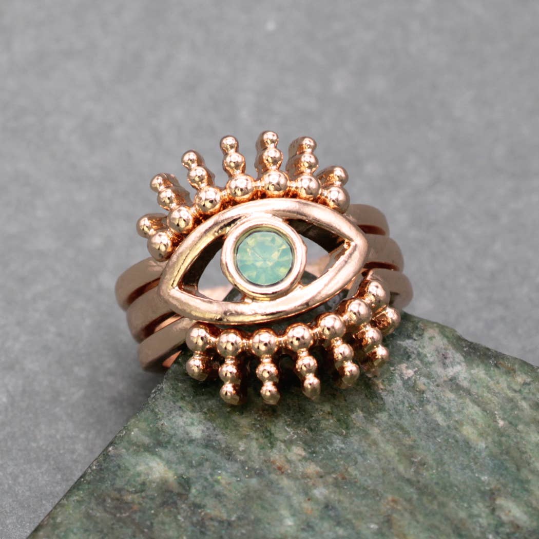 Rose gold ring with eye design and turquoise stone on a gray background