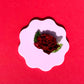 Red rose hair clip on a white circular piece of paper with a scalloped edge, against a red background