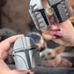 Two hands holding gray and silver Mandalorian helmet-shaped hair claw clips