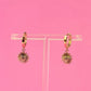 Gold hoop earrings with sunray shaped charms on a clear stand against a pink background