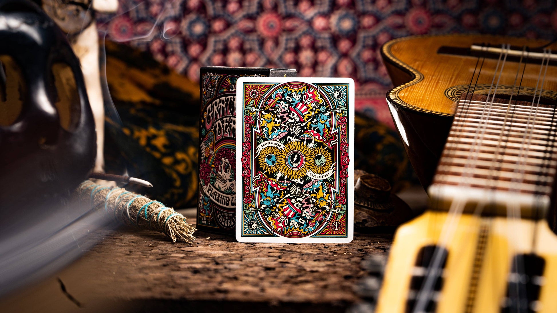 Colorful playing card box with intricate design on a wooden surface with musical instruments in the background.