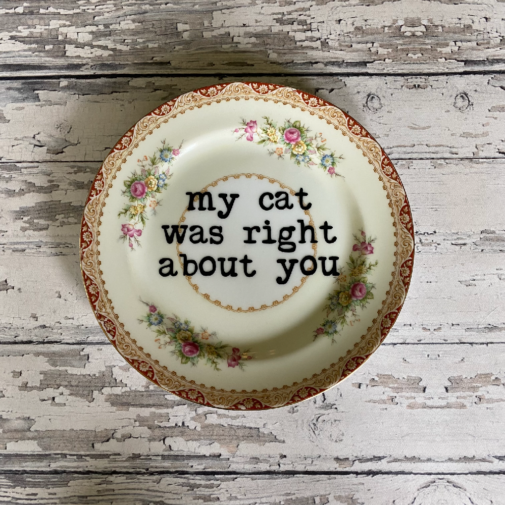 Decorative plate with floral design and text 'my cat was right about you' on a wooden surface
