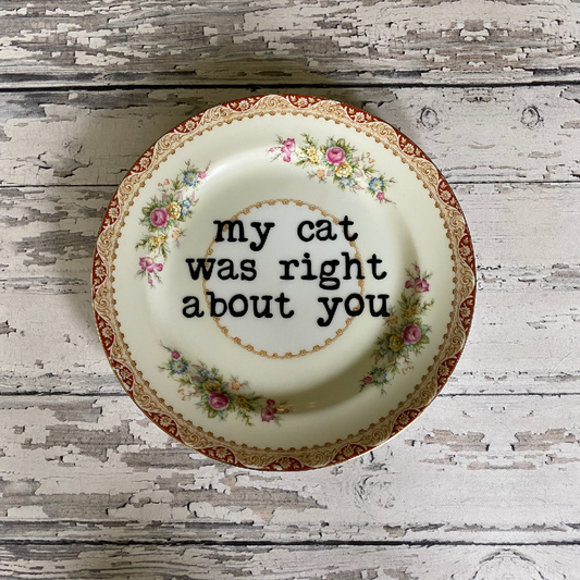 Decorative plate with floral design and text 'my cat was right about you' on a wooden surface