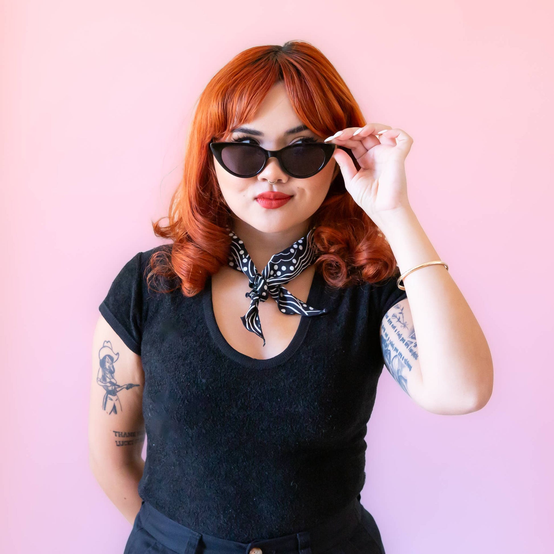 Woman with red hair wearing sunglasses against a pink background