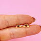 Rainbow-shaped earrings held between fingers against a pink background