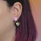 Close-up of an ear with a pink heart earring and a coffee cup earring against a blurred background.