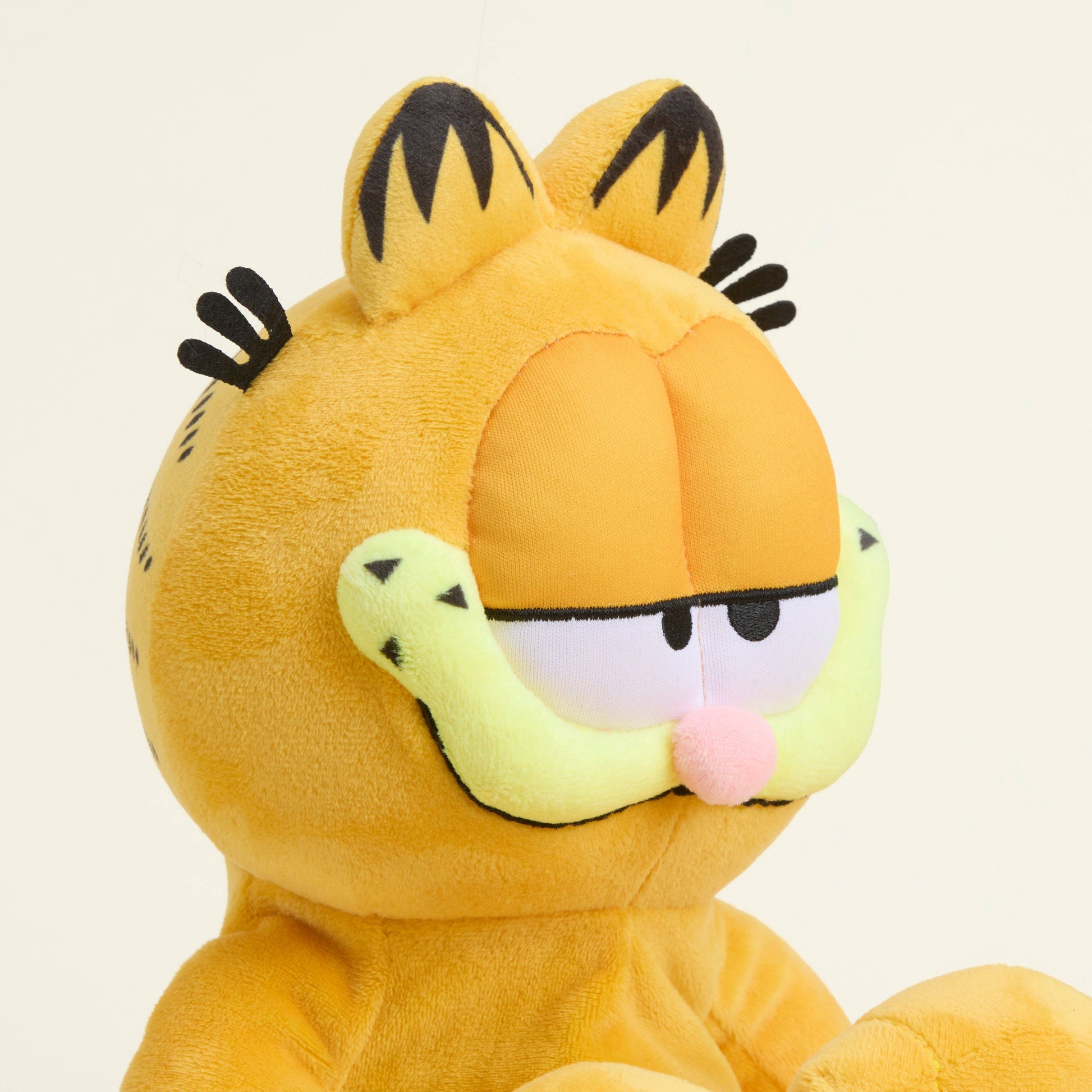 Plush toy of a cartoon cat character Garfield with a neutral expression on a beige background