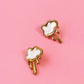 Pair of gold earrings with white cloud designs on a pink background