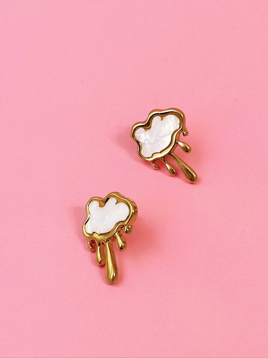 Pair of gold earrings with white cloud designs on a pink background