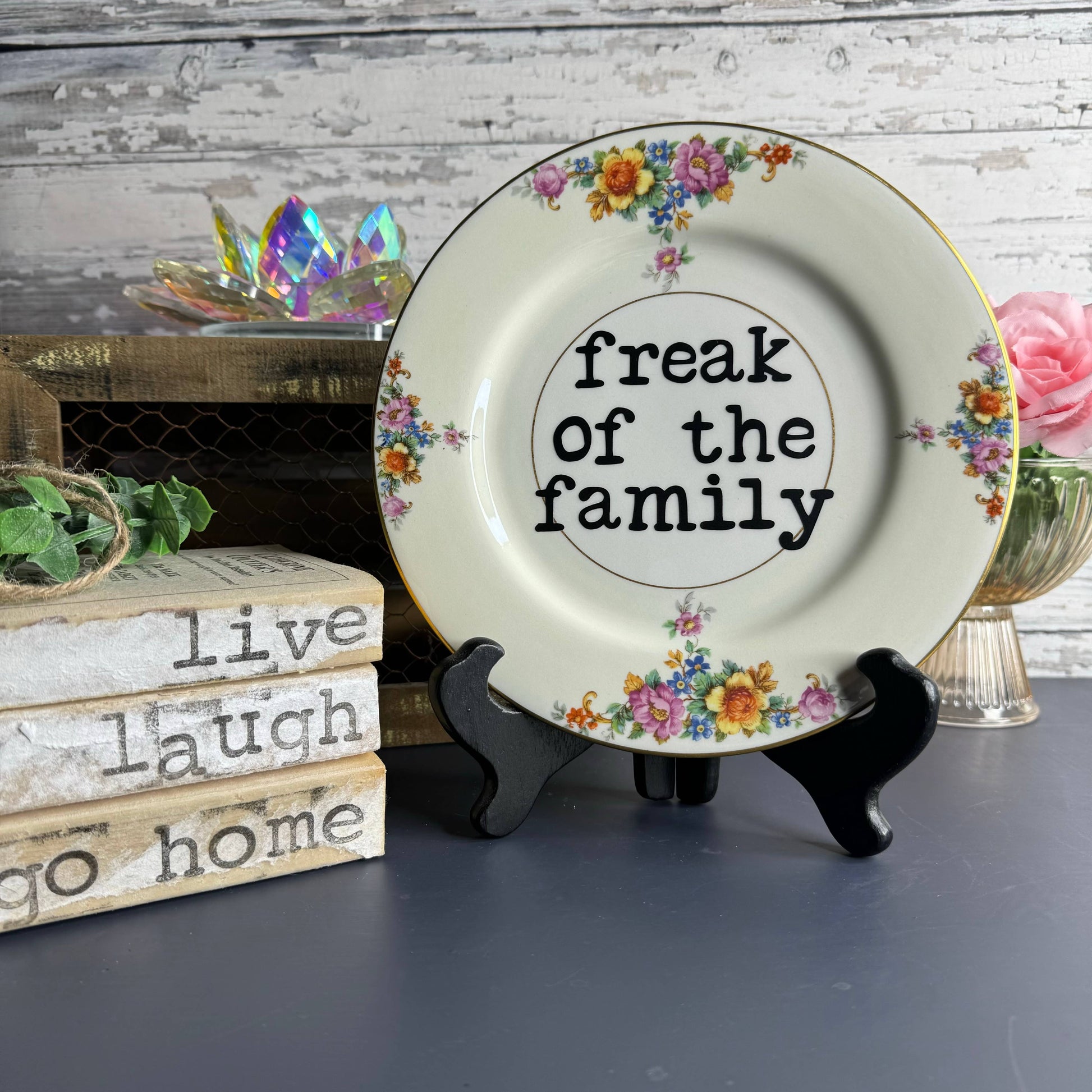 Decorative plate with floral designs and text 'freak of the family' on a stand.