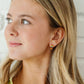 Woman wearing rainbow earrings with a neutral background