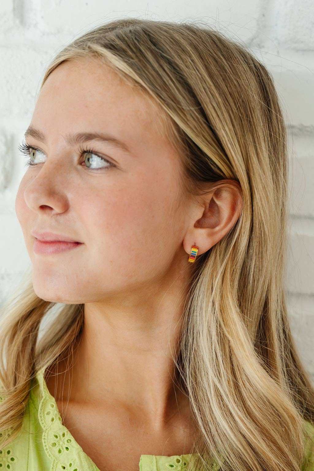 Woman wearing rainbow earrings with a neutral background