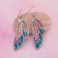 Pair of wing-shaped earrings with a colorful design on a pink background