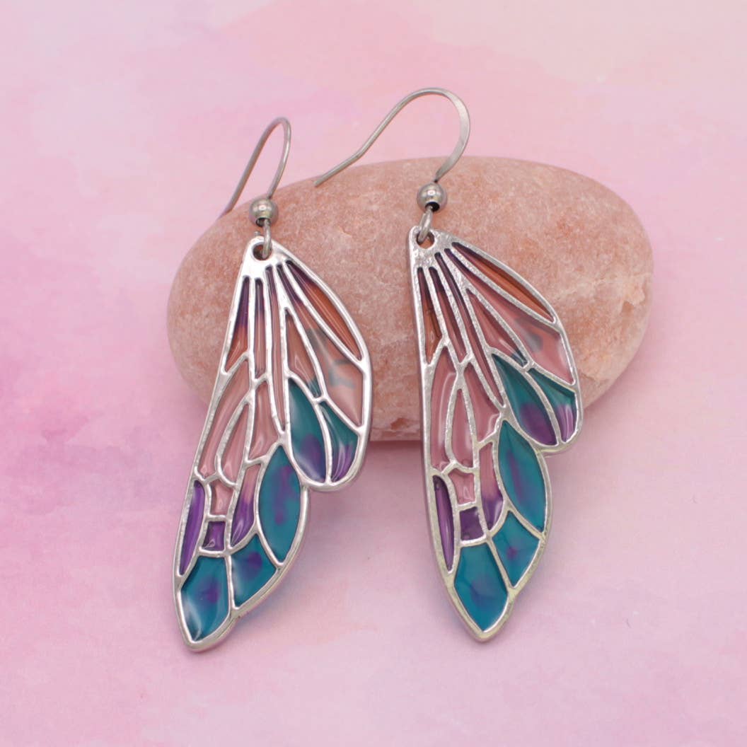 Pair of wing-shaped earrings with a colorful design on a pink background
