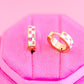 Two gold pink checkered hoop earrings on a pink textured surface